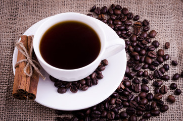 Coffee in a white cup with cinnamon sticks on a burlap background