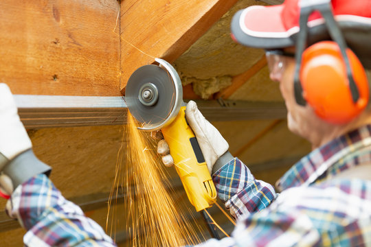 Man Fixing Metal Frame Using Angle Grinder On Attic Ceiling Covered With Rock Wool