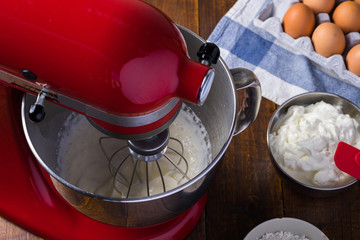 mixing red standing mixer kitchen aid on wooden table with cream cheese eggs glass flower