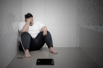 Depressed fat man sitting with a scale