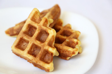 Belgian waffles in white plate. Healthy breakfast close up, pieces of freshly baked classic wafer