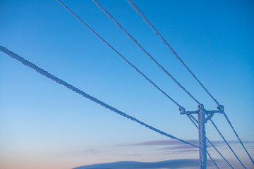 Frost and snow covered power lines during very cold winter against sky