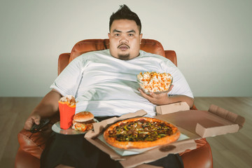 Obese man watching TV with junk foods at home