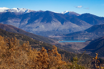 Lake in valley surrounded by mountains, trees in foreground.