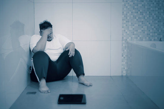 Sad Fat Man Sits With A Scale In The Bathroom