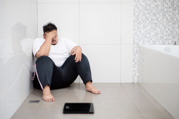 Stressed fat man sitting with a scale