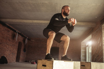 Caucasian determined sportsman performing plyometric box jumps indoor, in crossfit functional...