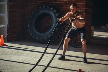 Fototapeta na wymiar Hard work of Crossfit instructor of caucasian ethnicity proves that training ropes are a very dynamic workout that accelerates athlete's pulse while strengthening his body.
