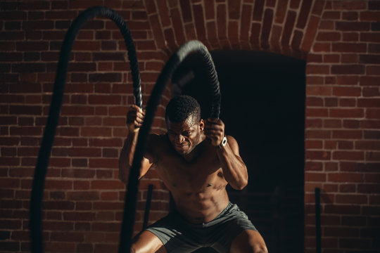 Hard work of Crossfit instructor of African ethnicity proves that training ropes are a very dynamic workout that accelerates athlete's pulse while strengthening his body. - Powered by Adobe