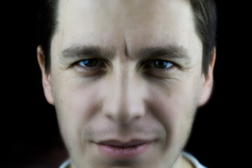 Confident man close up. Male face closeup on a black background. Studio photo of a male face with skin texture, wrinkled eyes and a crease between the eyebrows.