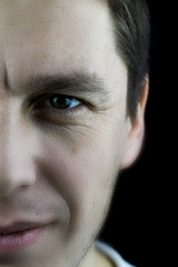 Obraz premium Left half of the face of a confident man close up. Fragment of a male face close-up on a black background. Studio photo of a male face with skin texture, wrinkled eyes.