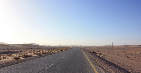Fototapeta premium Highway through scenic desert of Jordan. High voltage powerlines along asphalt road in arid valley. Early morning in wilderness after sunrise. Electric power poles. Horizontal.