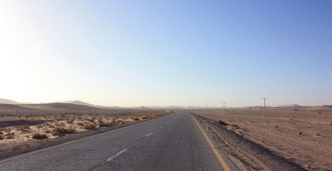 Highway through scenic desert of Jordan. High voltage powerlines along asphalt road in arid valley. Early morning in wilderness after sunrise. Electric power poles. Horizontal.