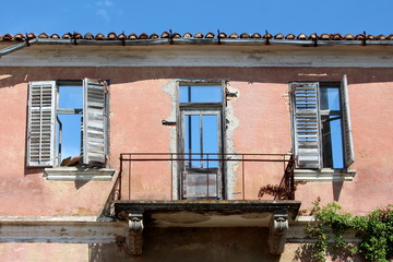 House ruins front wall with cracked destroyed facade and balcony with clear blue sky in background also seen through doors and windows on warm sunny day