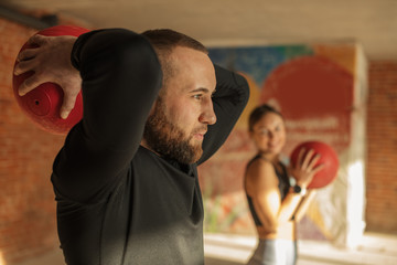 athletic sportsman and sportswoman doing exercises with medicine balls together in gym.