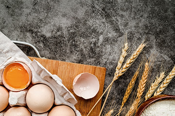 Baking ingredients with scattered flour on dark background with copyspace