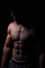 Fototapeta na wymiar Attractive African male fighter or boxer posing shirtless, isolated over dark background. Toned and ripped muscle fitness man under dramatic low key lighting, copy space.