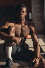 Fototapeta na wymiar Handsome African American bodybuilder man, with naked muscular torso posing against red brick wall.