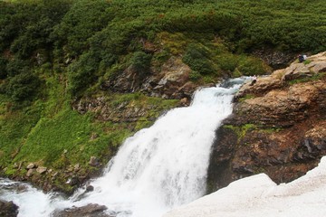 Beautiful waterfall on the mountain river Tahkoloch (or Klyuchevaya) in the caldera of an extinct Vachkazhets volcano on the Kamchatka Peninsula, Russia. Tourist is visible on the top of waterfall.