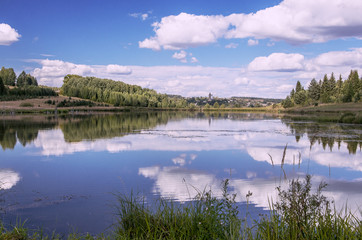 Summer view of the water surface of the river with overgrown picturesque banks and Cumulus clouds in the blue sky, toned.
