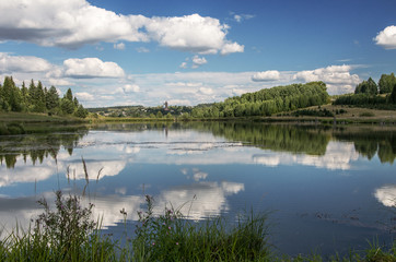 Summer view of the water surface of the river with overgrown picturesque banks and Cumulus clouds in the blue sky.