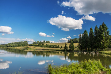 Summer view of the water surface of the river with overgrown picturesque banks and Cumulus clouds...