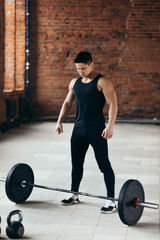 Fototapeta na wymiar strong muscular guy is standing nera the barbell and looking at it. preparation for training, concentration before workout. full length photo.