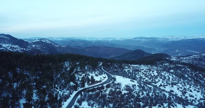 top view aerial drone flying above curvy road wind mountains and forest covered with snow on bad weather.