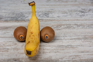 Banana and two kiwi with eyes on a white wooden background. Penis. Front view, space for text. Copy...