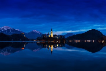 Fototapeta premium Beautiful view of famous Bled Island (Blejski otok) at scenic Lake Bled with Bled Castle (Blejski grad) and Julian Alps in the background in golden morning light at sunrise in summer, Slovenia 