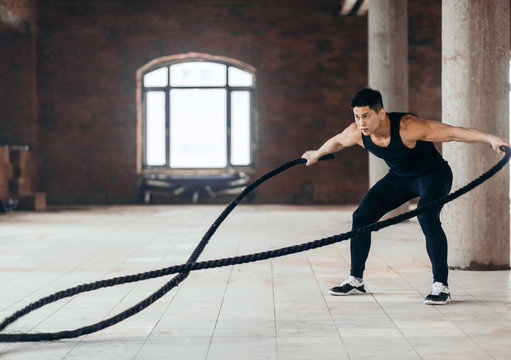 modern workout tool. awesome athlete develops muscles and cardio with battling rope. side view full length photo. copy space