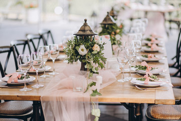 plates and glasses stand on the festive table, the table is decorated with flower compositions and cloth