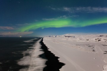 Aurora borealis, Iceland. Green northern lights. Starry sky with polar lights. Night winter landscape with aurora, sea with sky reflection and snowy mountains and black beach. Nature background 