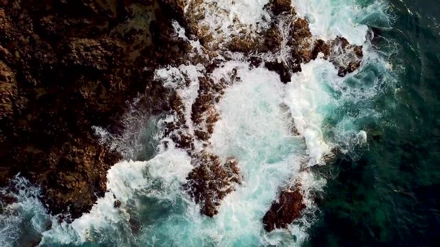 Top view vertical position of big waves going on the rocks at the beach - coast landscape from above with ocean water and rocky coast - outdoor nature dangerous and beautiful concept