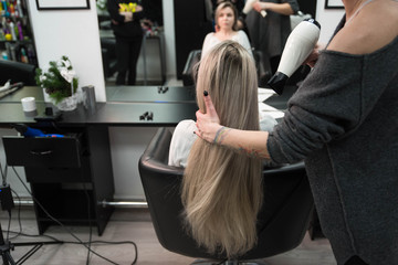 Professional hairdresser drying woman's hair with hairdryer in beauty salon