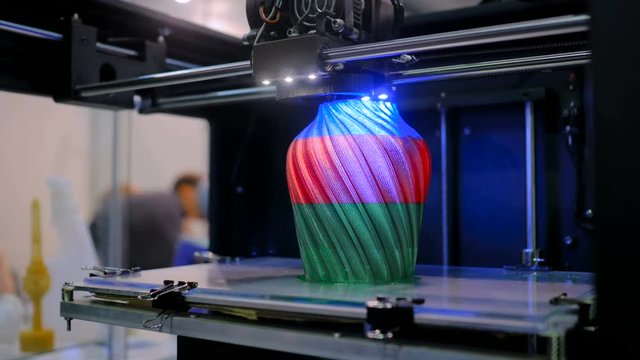 3D printer prints physical 3D model of tricolor vase with plastic wire filament at modern technology exhibition. Additive technologies, science and futuristic concept