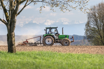 bauer sitzt auf traktor und fährt mit einer egge