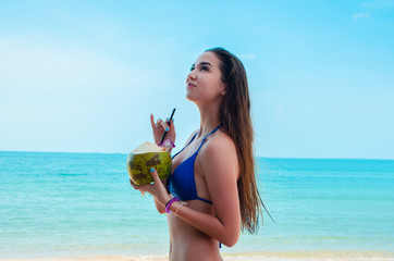  Young beautiful woman in blue bikini with long hair drinking fresh coconut on the beach