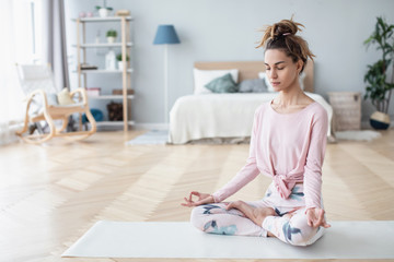 Portrait of attractive young woman working out at home, doing yoga exercise on white mat.