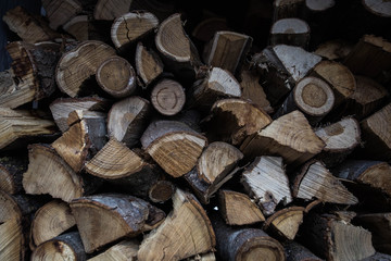 Wall of stacked wood logs as background dark shadows