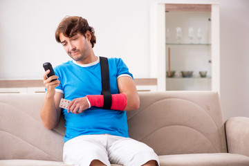 Young man with injured arm sitting on the sofa 