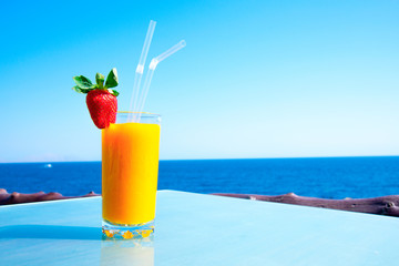 Fresh organic mango decorated with strawberries in a cafe by the sea. Fruit smoothie on the sea holiday. Vertical orientation with space for text.