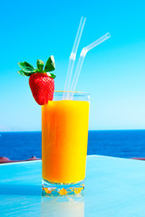 Fresh organic mango decorated with strawberries in a cafe by the sea. Fruit smoothie on the sea holiday. Horizontal orientation.Vitamin drink from fresh tropical fruits.