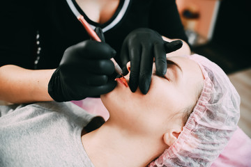 Permanent make-up for red Lips of beautiful woman in beauty salon. Closeup beautician doing tattooing Lips.