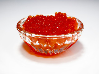 Salmon red caviar is laid out in a glass dish. Photographed on a light background.