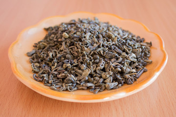 Green tea in a saucer on the table. Tea leaves, crushed, processed and ready to brew.
