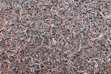 The dried, ready-to-drink black tea leaves are scattered on the table in a thin layer. Backgrounds, textures.