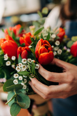 Woman florist makes a orange tulips bouquet on wooden table - 249837027