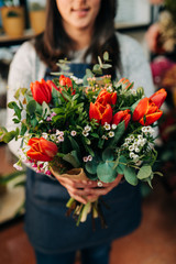 Woman florist makes a orange tulips bouquet on wooden table