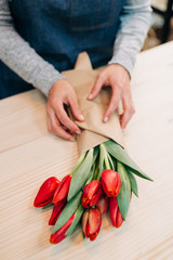 Obraz na płótnie Canvas woman florist makes red tulip bouquet and wrapping in pack paper on wooden table. Flowers